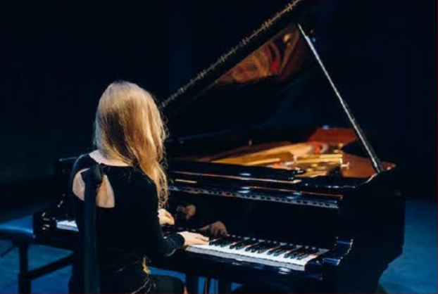 blonde Studentin im schwarzen Abendkleid spielt auf einen schwarzen Flügel